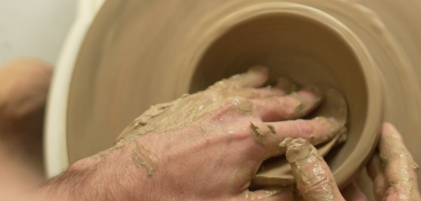 Foto de uma mão esculpindo um objeto de barro e argila.